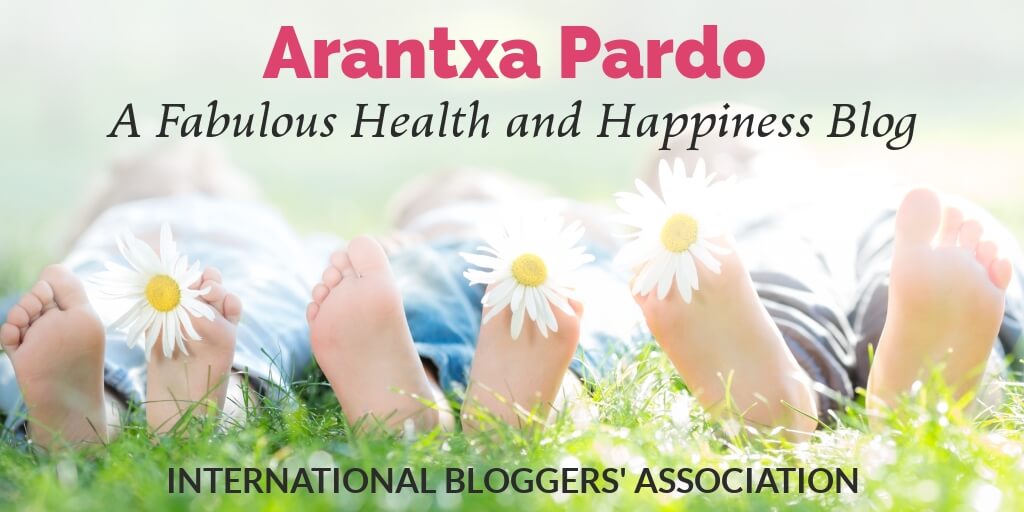 Laying in grass with daisy in toes and text overlay 'Arantxa Pardo - A Fabulous Health and Happiness Blog' by International Bloggers' Association